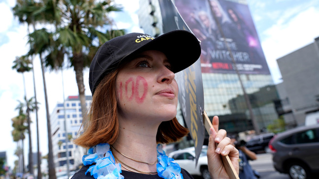 FILE - SAG-AFTRA member Emily Kincaid dons a 100 on her face as she carries a sign on a picket line outside Netflix studios on Wednesday, Aug. 9, 2023, in Los Angeles. The Hollywood writers strike reached the 100-day mark today as the U.S. film and television industries remain paralyzed by dual actors and screenwriters strikes. (AP Photo/Chris Pizzello)